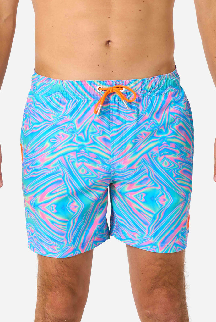 Man wearing a men's vibrant holographic swim shorts with a mesmerizing blue, pink, and purple swirl design. Eye-catching and stylish swimwear for summer fun. Closeup of his middle.