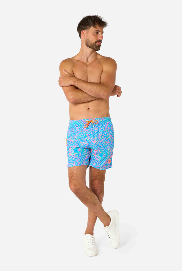 Man wearing a men's vibrant holographic swim shorts with a mesmerizing blue, pink, and purple swirl design. Eye-catching and stylish swimwear for summer fun. Full body image looking side ways.