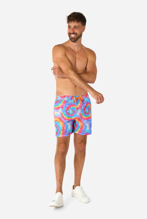 Man wearing a men's rainbow tie-dye swim shorts with a bold, colorful spiral pattern. A fun and trendy choice for beach days and pool parties. Full body image.