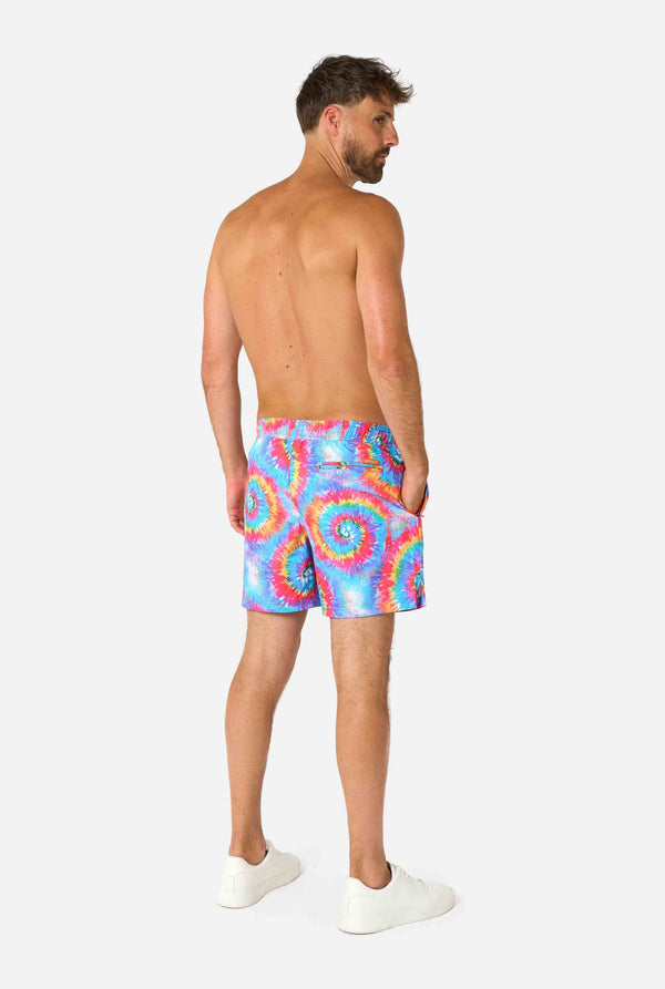 Man wearing a men's rainbow tie-dye swim shorts with a bold, colorful spiral pattern. A fun and trendy choice for beach days and pool parties. View from the back.
