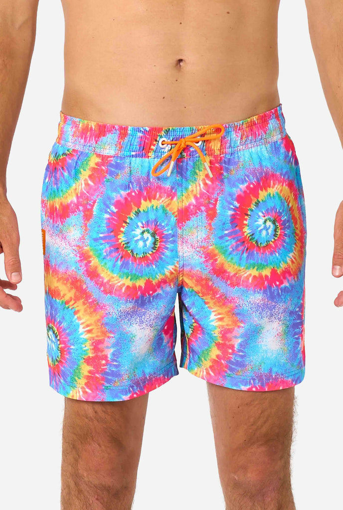 Man wearing a men's rainbow tie-dye swim shorts with a bold, colorful spiral pattern. A fun and trendy choice for beach days and pool parties. Close-up middle.