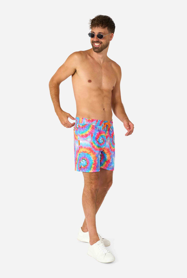 Man wearing a men's rainbow tie-dye swim shorts with a bold, colorful spiral pattern. A fun and trendy choice for beach days and pool parties. Full body image and wearing sunglasses.