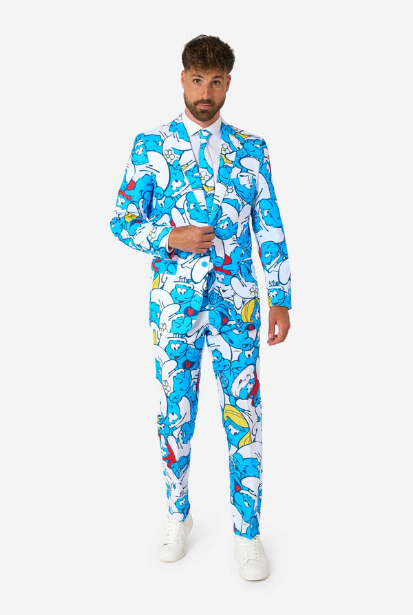 Man wearing a colorful Smurfs men's suit with an all-over cartoon print in blue, white, red, and yellow, including a matching tie and white shirt, standing against a plain background. Full body image.