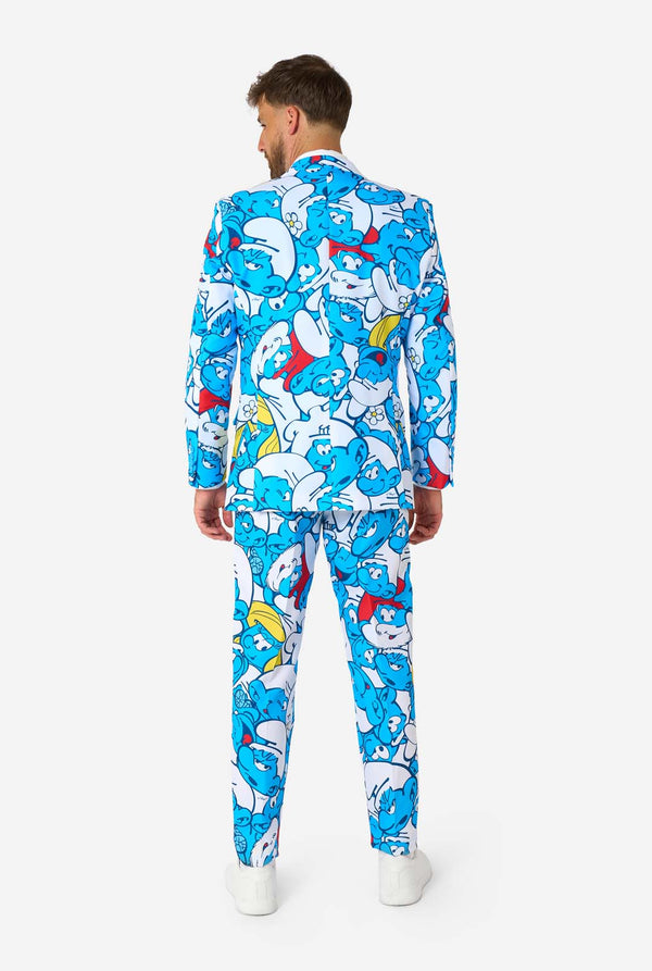 Smiling man wearing a colorful Smurfs men's suit with an all-over cartoon print in blue, white, red, and yellow, including a matching tie and white shirt, standing against a plain background. View from the back.