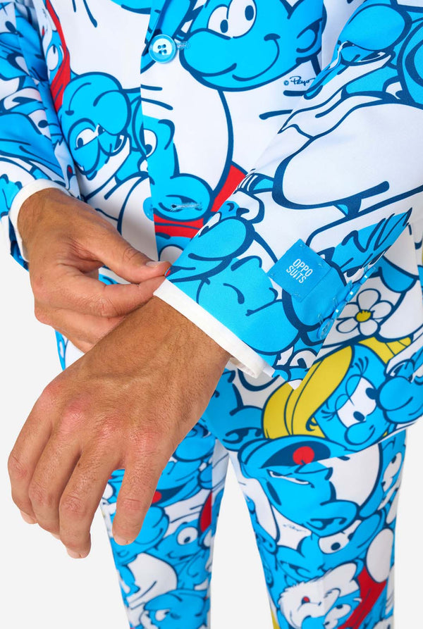 Man wearing a colorful Smurfs men's suit with an all-over cartoon print in blue, white, red, and yellow, including a matching tie and white shirt, standing against a plain background. Sleeve close up.