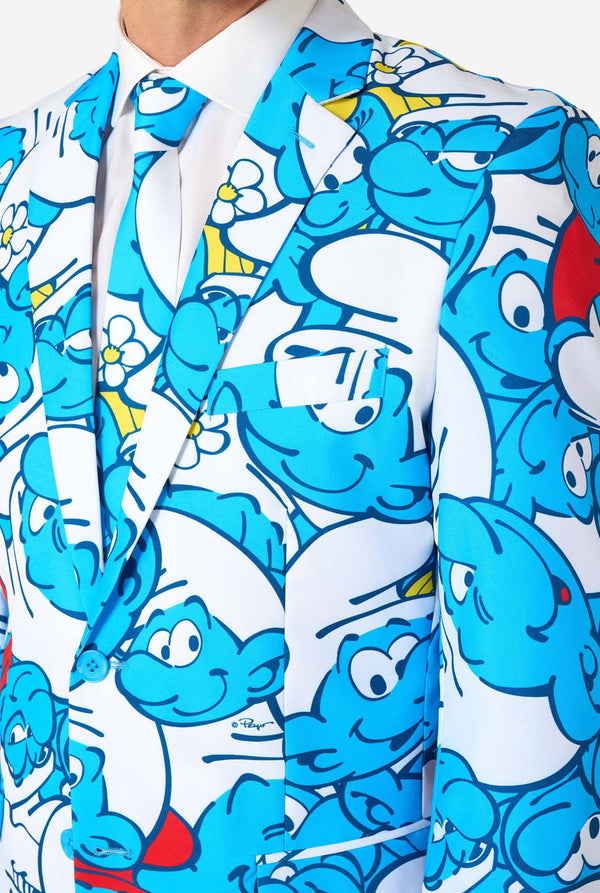 Man wearing a colorful Smurfs men's suit with an all-over cartoon print in blue, white, red, and yellow, including a matching tie and white shirt, standing against a plain background. Chest close up.