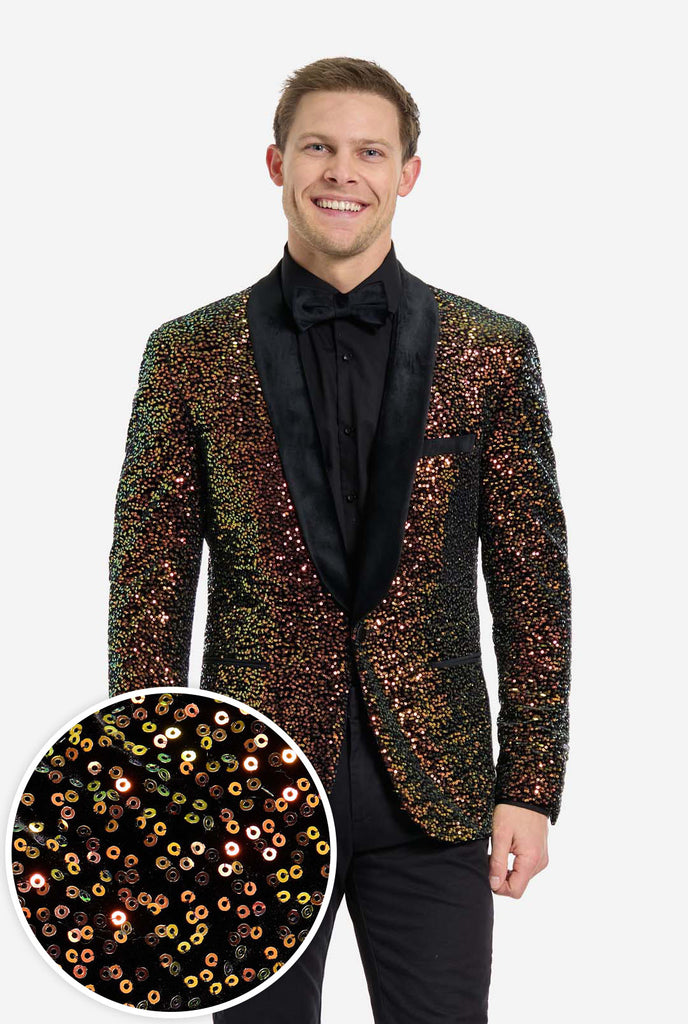 A man is standing and smiling, dressed in a formal, eye-catching outfit. He is wearing a black dress shirt with a black bow tie and a blazer adorned with shimmering amber-colored sequins that reflect light in various shades of gold, copper, and green. The blazer has a satin black shawl collar and front pockets. He pairs this bold jacket with black dress pants. The background is plain, emphasizing the dazzling effect of the sequined blazer. Including close up round in left corner.