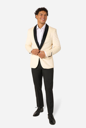 Man wearing a cream blazer with black lapels and black pants on a light background. Full body image.