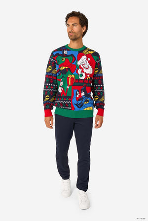 Full-body view of a man in a Batman-themed knitted Christmas sweater, paired with navy trousers and white sneakers.