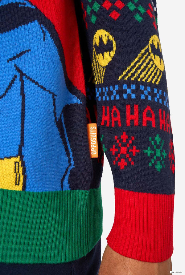 Close-up of the knitted Christmas sweater hem with Batman motifs, red and green ribbed cuffs, and an orange “Opposuits” label.