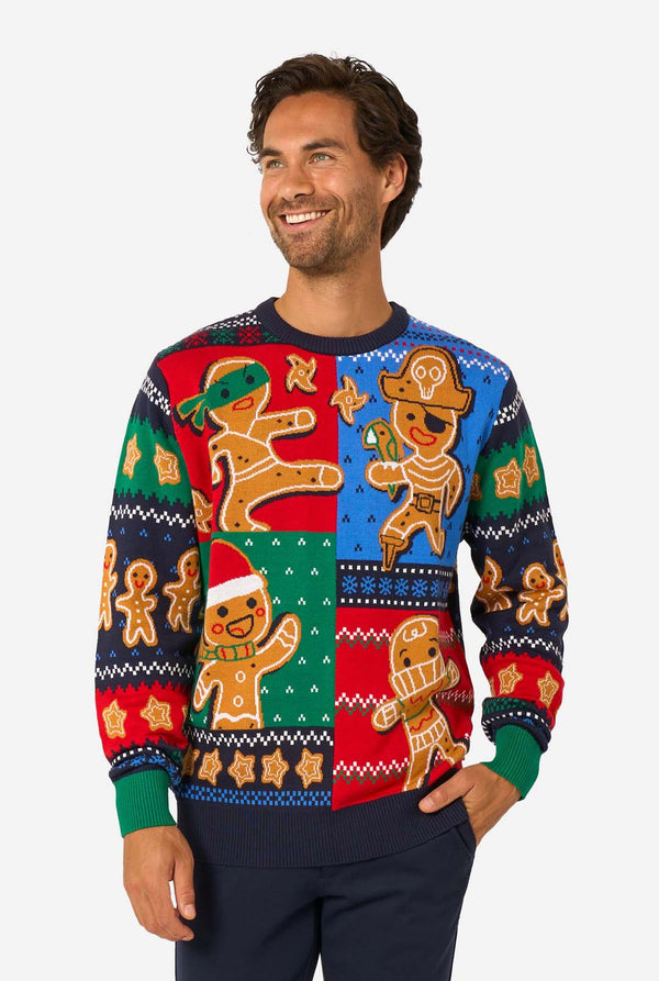 Smiling man wearing a colorful knitted Christmas sweater featuring gingerbread characters on red, green, and blue panels.