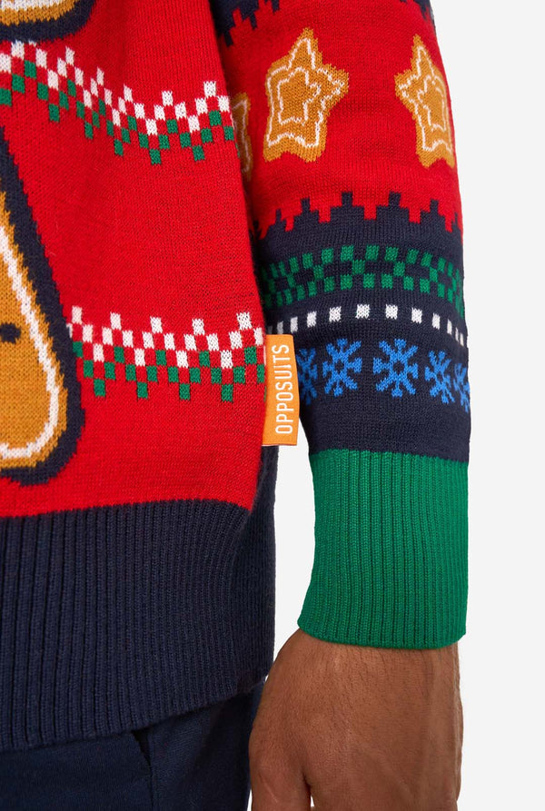 Close-up of the knitted Christmas sweater hem with an orange “Opposuits” label and green ribbed cuff.