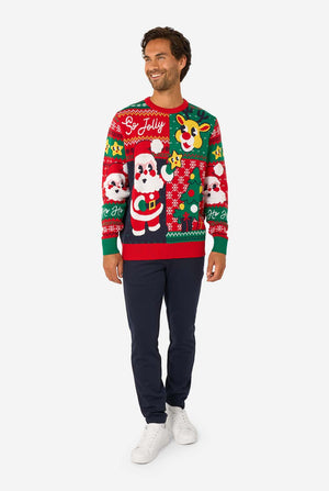 Full-body view of a man in a red and green knitted Christmas sweater with Santa and reindeer designs, navy trousers, and white sneakers.