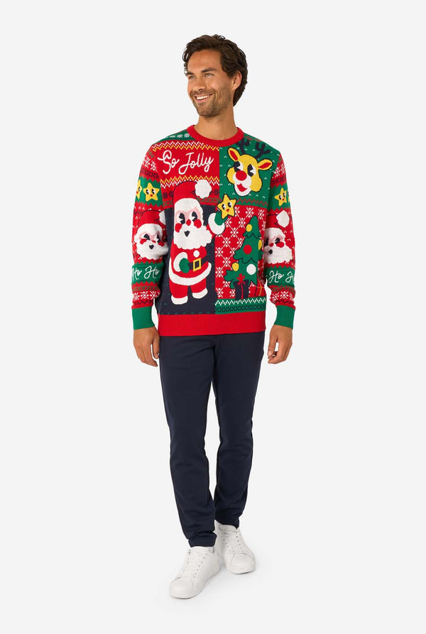 Full-body view of a man in a red and green knitted Christmas sweater with Santa and reindeer designs, navy trousers, and white sneakers.