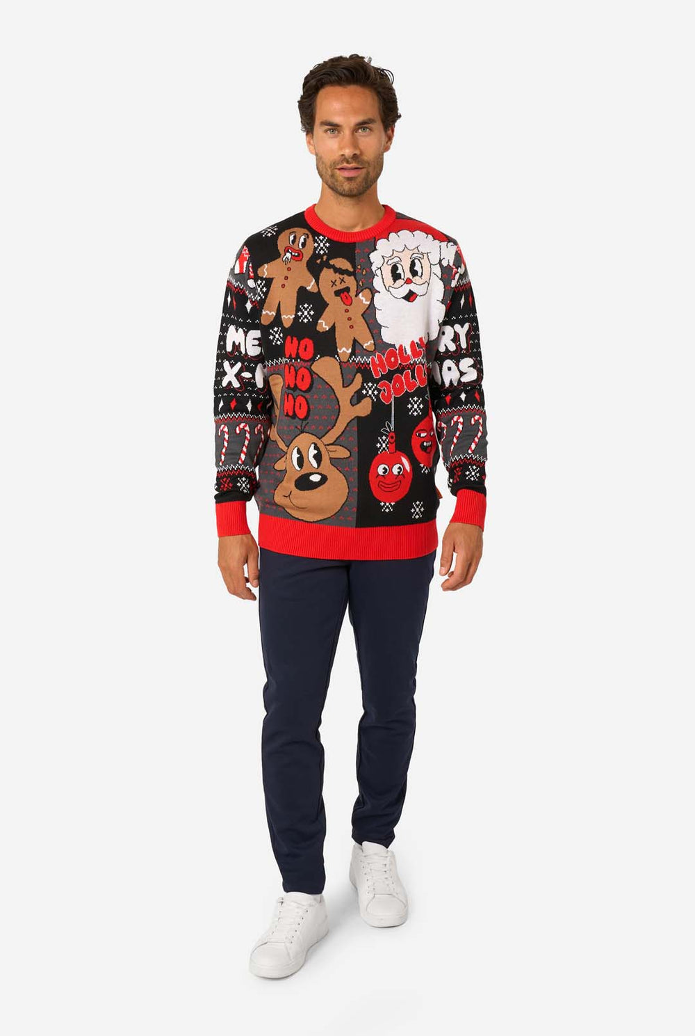 Smiling man wearing a black and red knitted Christmas sweater featuring Santa, reindeer, gingerbread men, and festive ornaments.