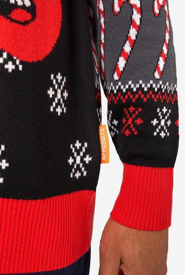 Close-up of the knitted Christmas sweater hem featuring red ribbed cuffs, snowflake patterns, and an orange “Opposuits” label.