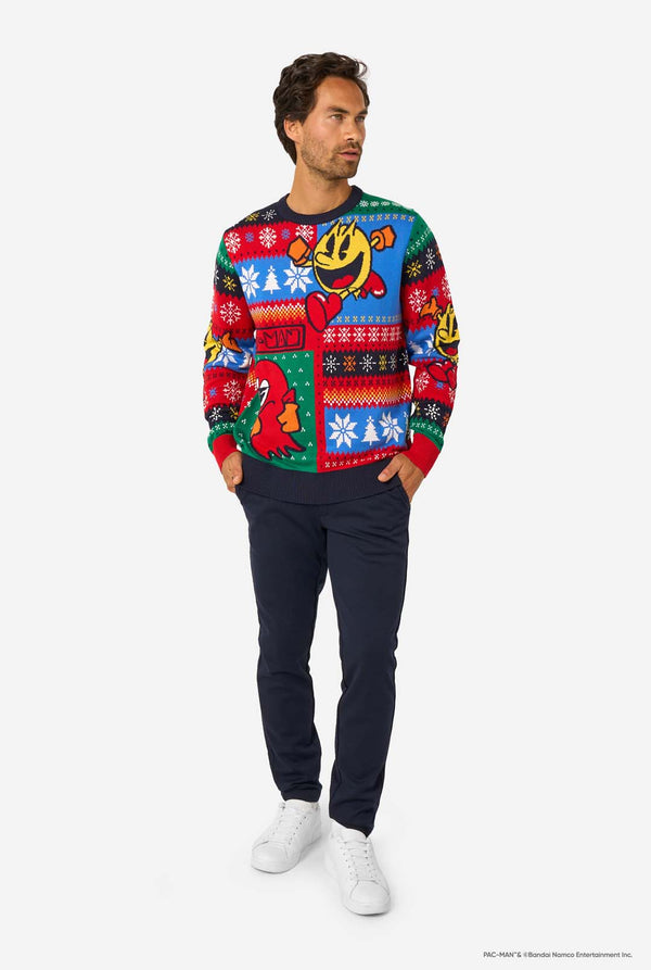 Full-body view of a man in a Pac-Man-themed knitted Christmas sweater, navy trousers, and white sneakers.