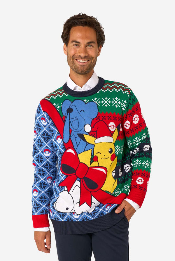 Smiling man wearing a colorful knitted Christmas sweater featuring Pikachu in a Santa hat with a red bow and festive patterns.