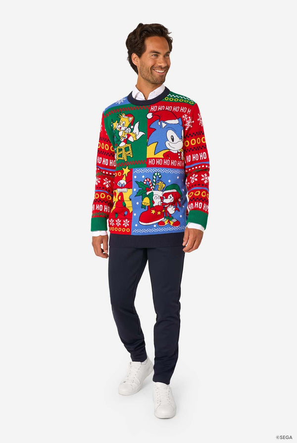 Full-body view of a man in a Sonic-themed knitted Christmas sweater, navy trousers, and white sneakers.