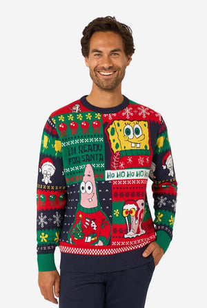 Smiling man wearing a colorful knitted Christmas sweater featuring SpongeBob, Patrick, and other festive cartoon characters.