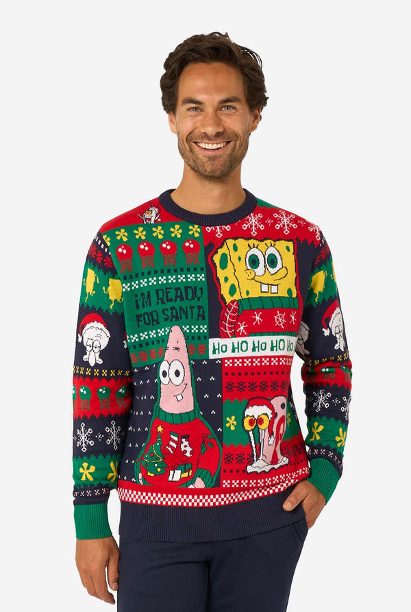 Smiling man wearing a colorful knitted Christmas sweater featuring SpongeBob, Patrick, and other festive cartoon characters.