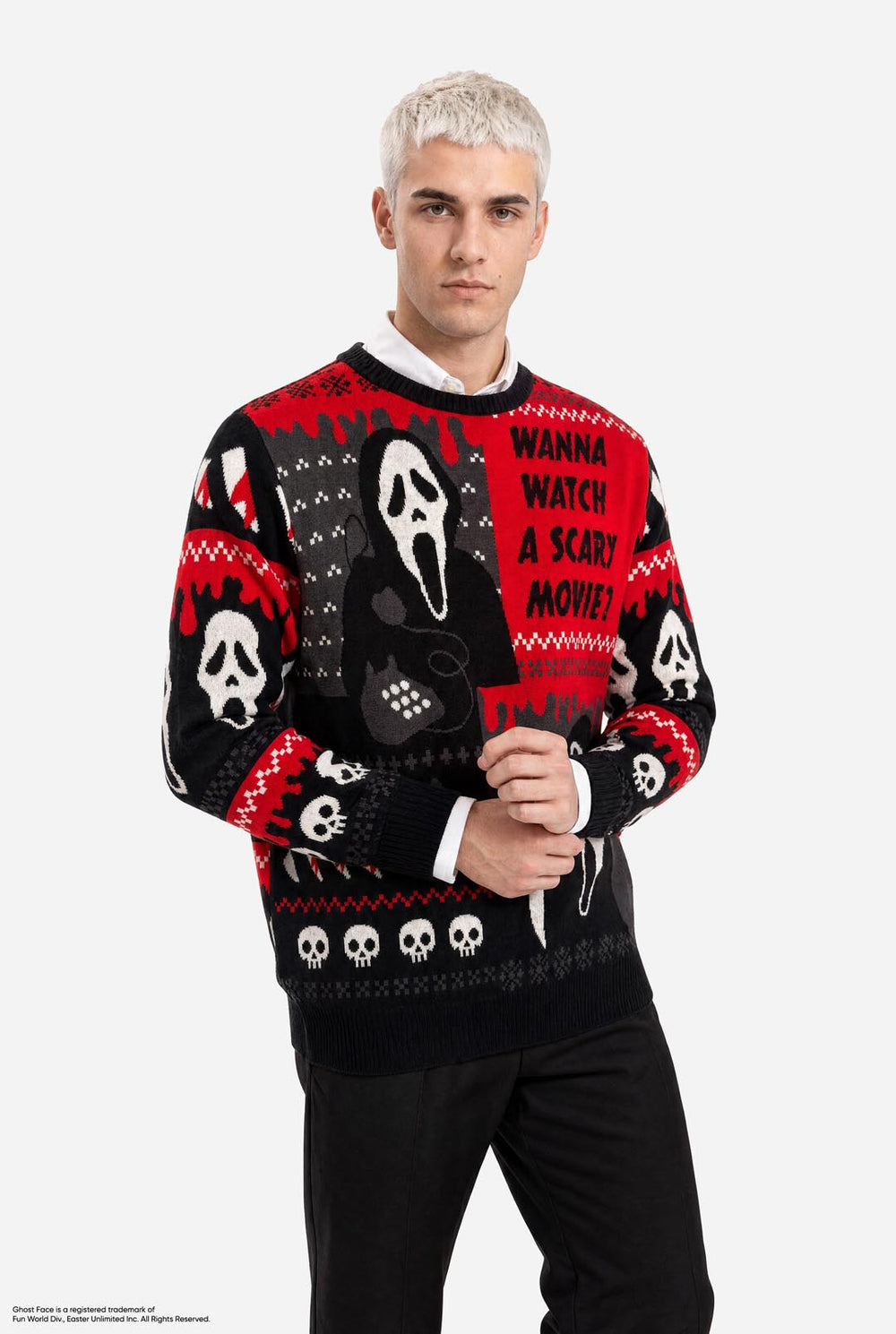 A male model with platinum blonde hair wearing a black and red Halloween sweater with Ghostface and skull graphics, standing against a light gray background.