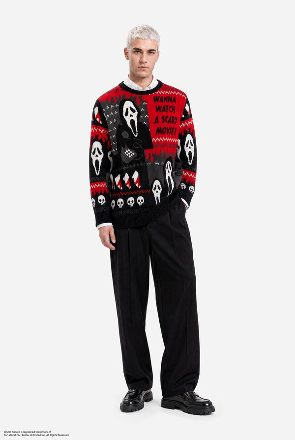 A male model wearing a black and red holiday sweater with Ghostface and 'I Wanna Watch A Movie' graphics, paired with black trousers and black shoes, against a light gray background.
