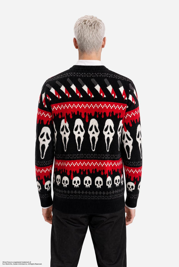 A man viewed from behind wearing a black knit sweater with a red and white horror-themed pattern featuring Ghostface masks and dripping red motifs, paired with black pants against a light gray studio background.