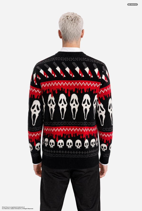 A male model with platinum blonde hair wearing a black and red Halloween-themed knit sweater with Ghostface and skull patterns, paired with black pants, against a light gray background. View from the back.