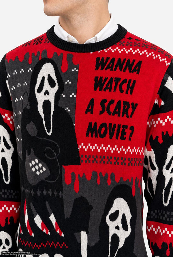 A male model wearing a black and red holiday sweater with Ghostface and 'I Wanna Watch A Movie' graphics,  against a light gray background. Chest close-up.