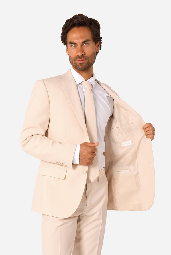 Image of a man wearing a sand colored beige suit and a white shirt. Holding one side of the jacket open.