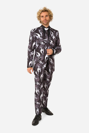 A man modeling a black and white Ghost Face-patterned suit with a black shirt, black tie, and black dress shoes, standing against a light gray background.