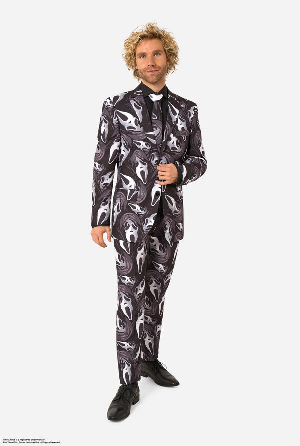 A man modeling a Ghostface-themed suit with a black, white, and gray mask pattern, a black shirt, a bow tie. Full-body image.
