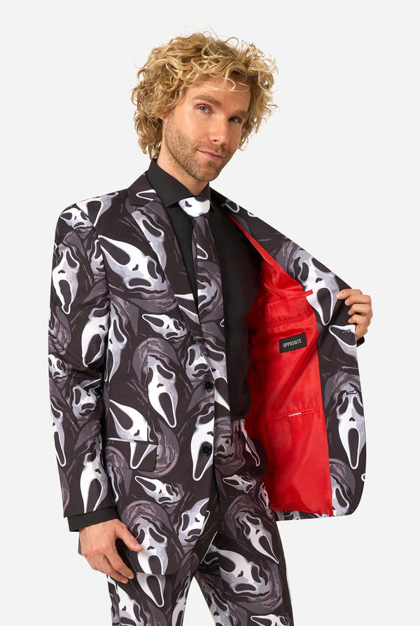A man modeling a Ghostface-themed suit with a black, white, and gray mask pattern, a black shirt, a white bow tie, and a bright red lining visible on the open jacket.