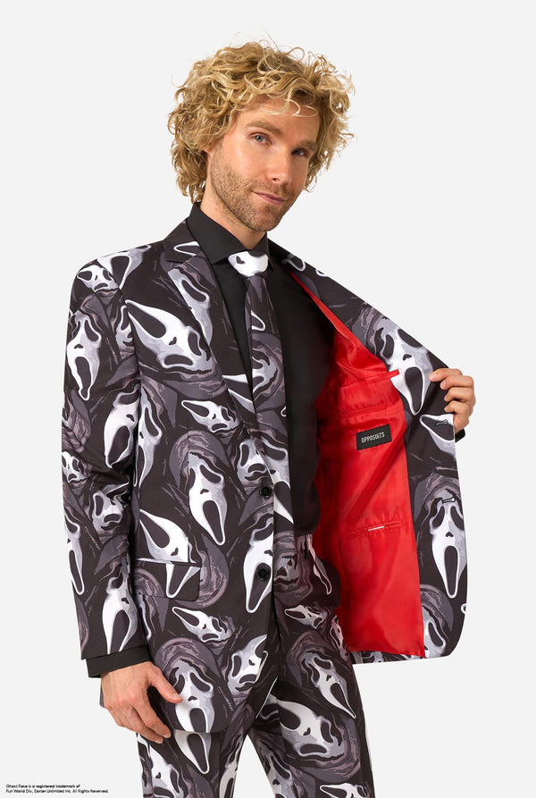 A man modeling a Ghostface-themed suit with a black, white, and gray mask pattern, a black shirt, a bow tie, and a bright red lining visible on the open jacket.
