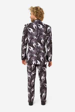 A man viewed from the back wearing a matching suit with an all-over white and gray shark pattern on a black background, set against a plain light gray studio backdrop.