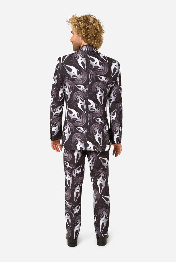 A man viewed from the back wearing a matching suit with an all-over white and gray shark pattern on a black background, set against a plain light gray studio backdrop.