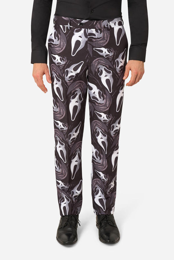 A person wearing black pants with an allover Ghostface-style mask print in white and gray, paired with a black long-sleeve top and black shoes, shown against a light gray studio background.