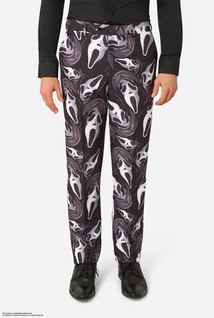 A person wearing black pants with an allover Ghostface mask print in white and gray, paired with a black long-sleeve top and black shoes, shown against a light gray studio background.