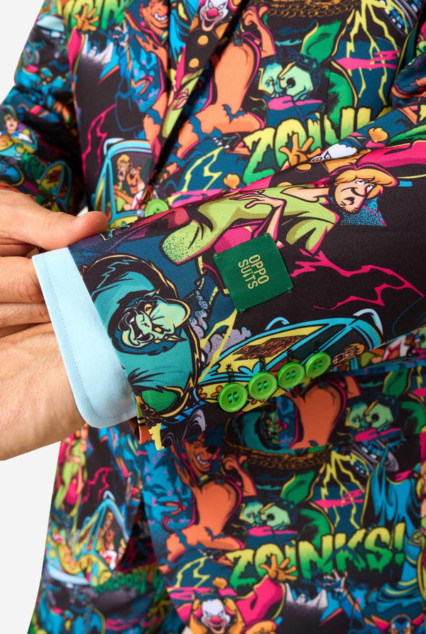 A sleeve close-up of a man wearing a vibrant, multicolored Scooby-Doo print suit jacket and matching tie. The pattern features various Scooby-Doo characters in bright neon colors on a dark background, styled with a light blue dress shirt.