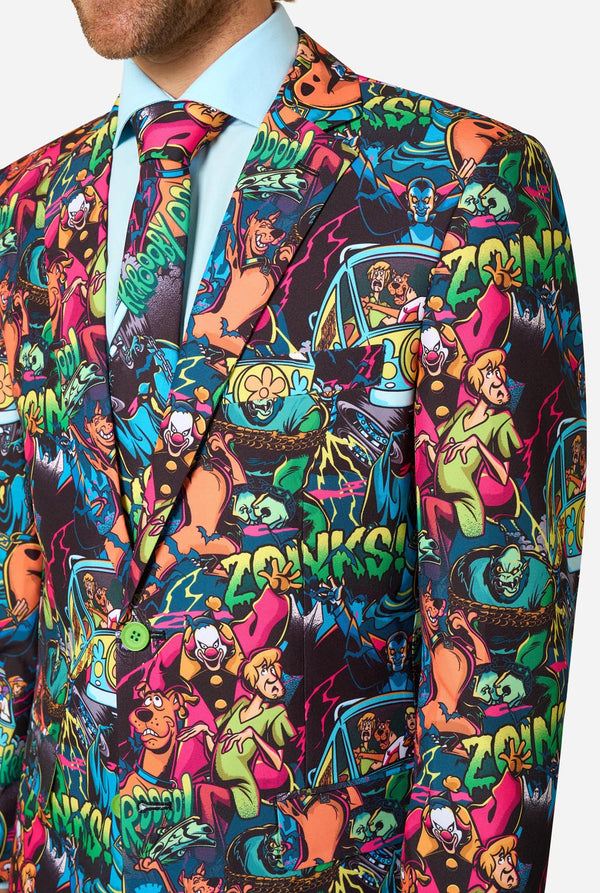 A close-up of a man wearing a vibrant, multicolored Scooby-Doo print suit jacket and matching tie. The pattern features various pop-culture characters in bright neon colors on a dark background, styled with a light blue dress shirt.