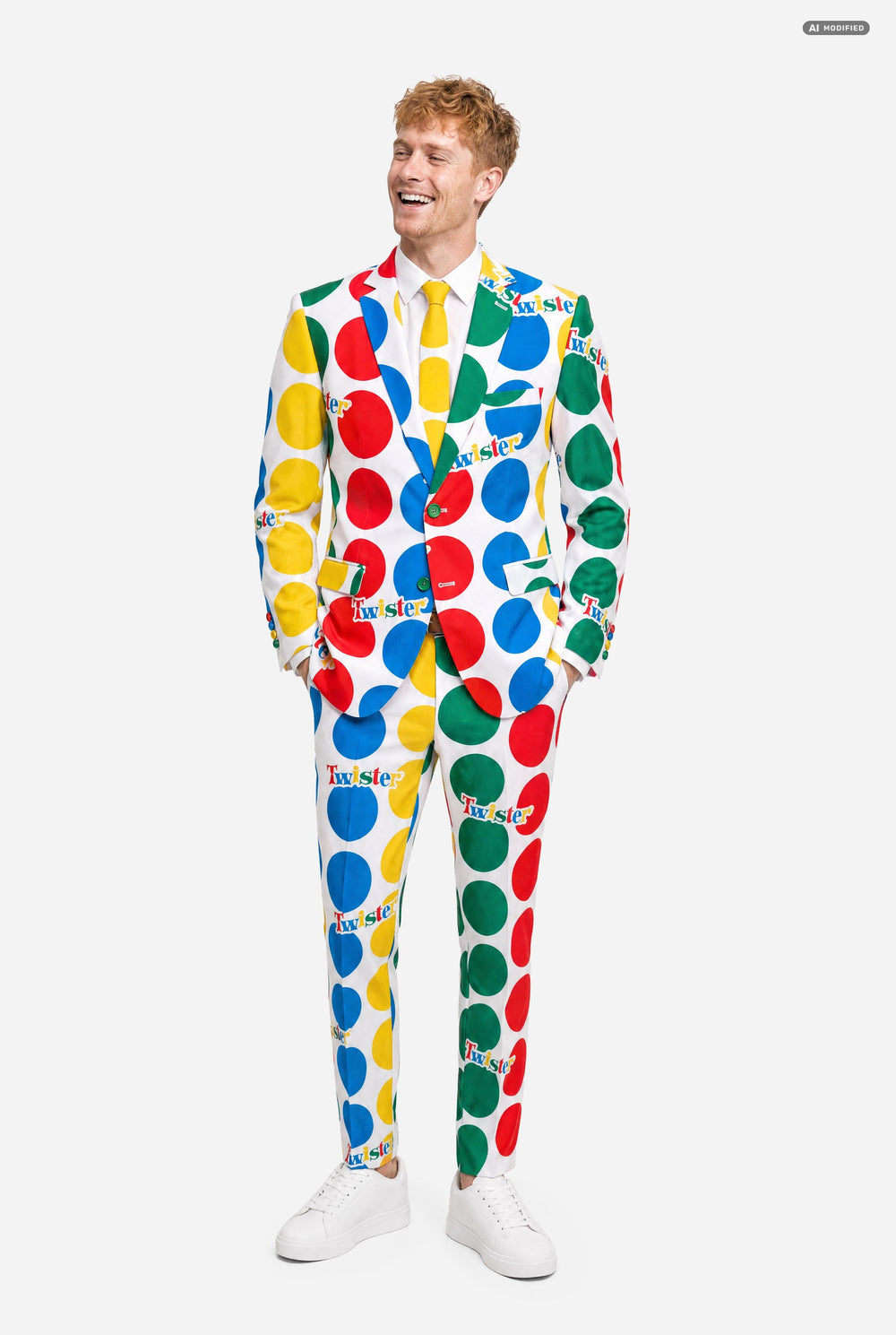 A man wearing a white suit with large multicolored polka dots and the Twister logo, resembling a Twister mat paired with a white and yellow tie, against a light gray studio background.