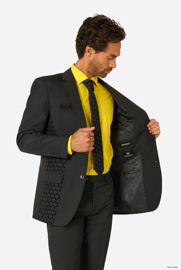 Man opening the black Batman suit jacket to show the inner lining and branding, worn with a yellow shirt and black tie.