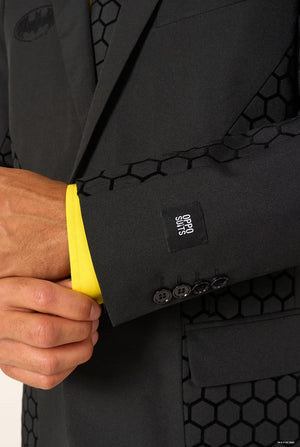 Close-up of the black Batman suit sleeve showing button details, hexagon-patterned fabric, and a yellow shirt cuff.