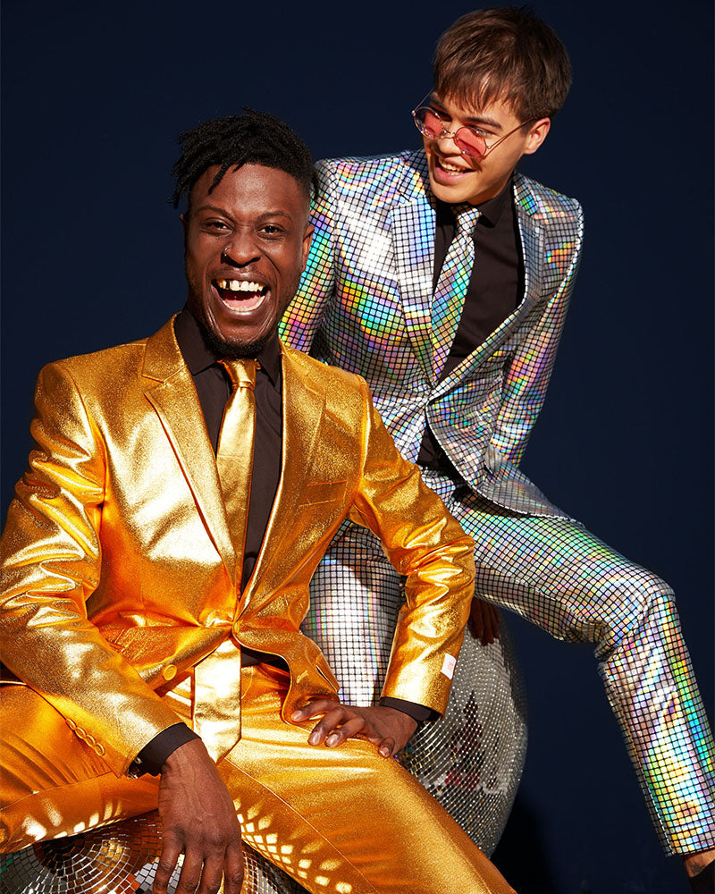 Two men posing in reflective metallic suits against a dark navy background. The man in the foreground wears a shiny gold suit with a gold tie and black shirt, while the man behind him wears a holographic silver check patterned suit over a black shirt.