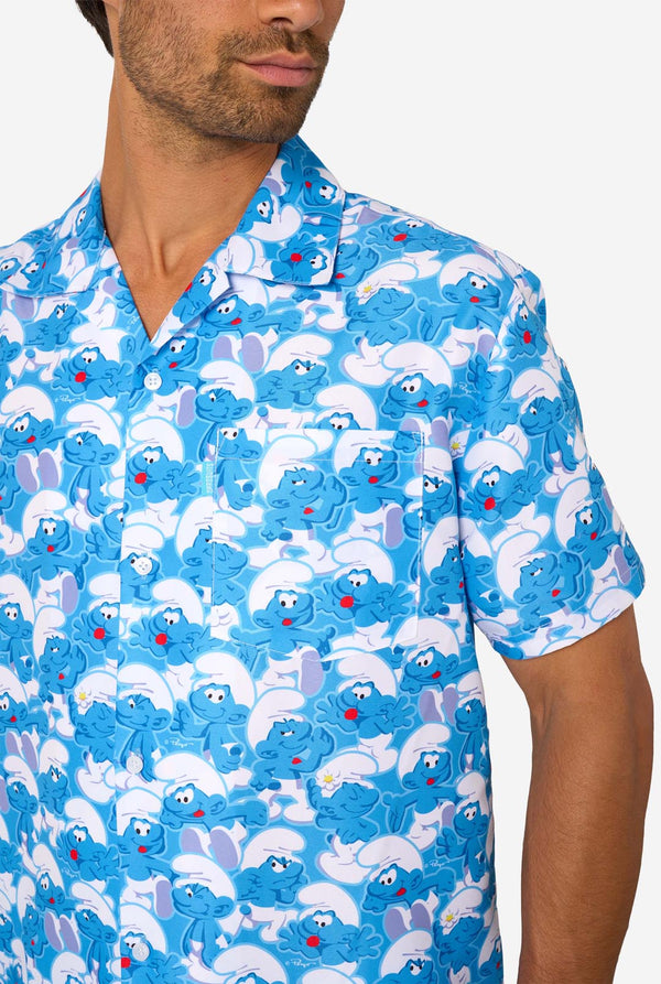 Man wearing a blue and white Smurfs patterned shirt and shorts on a light background. Chest close-up.