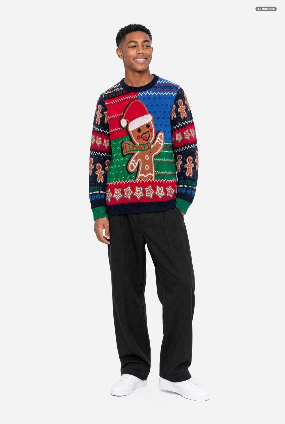 A young man wearing a festive Christmas sweater with a gingerbread man design, set against a plain light gray background.