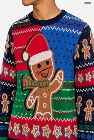 A close-up of a festive Christmas sweater featuring a large gingerbread man wearing a Santa hat and striped scarf on the front, with red, blue, green, and white holiday patterns across the body and sleeves.