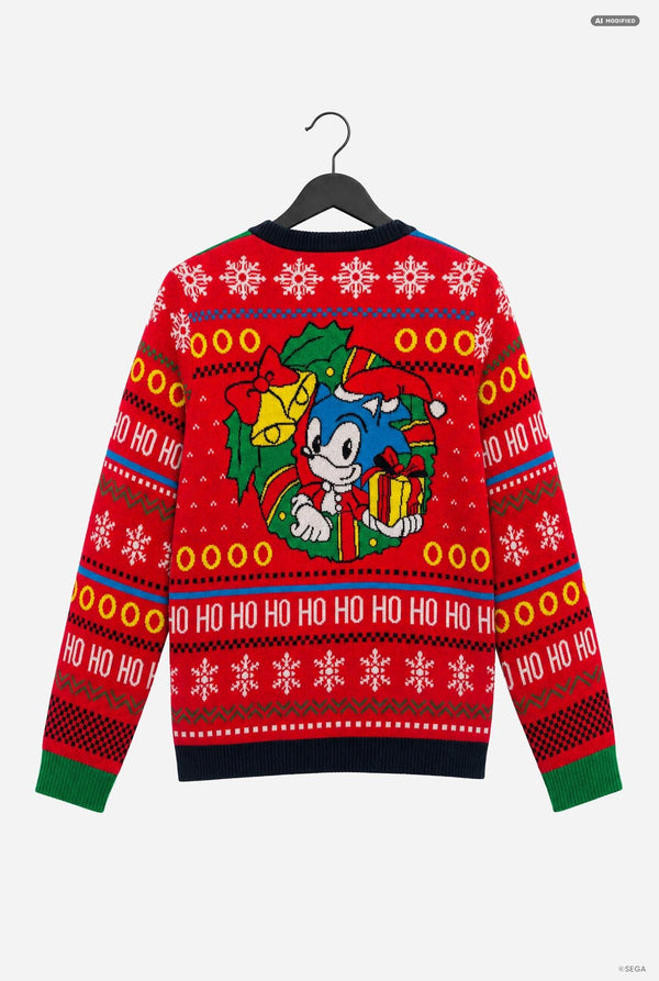A red Christmas sweater featuring Sonic the Hedgehog, hanging on a black hanger against a light gray background. The sweater has a festive pattern with snowflakes, 'HO HO HO' text, and a central graphic of Sonic wearing a Santa hat and holding a gift.