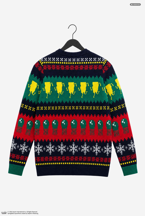 A festive Christmas sweater displayed on a black hanger against a light gray background. The back of the long-sleeve knit sweater features a multi-colored holiday pattern with rows of yellow lemons, green olives, red peppers, and white snowflakes on a dark navy base.